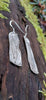 Sterling silver melt textured long drop earrings sitting on a mossy log.