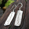 Sterling silver melt textured drop earrings sitting on a mossy log.