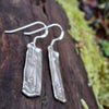 Sterling silver melt textured drop earrings sitting on a mossy log.