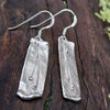Sterling silver melt textured drop earrings sitting on a mossy log.