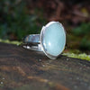 Silver ring with a soft green Amazonite oval stone on a log in the sunshine.