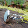 Silver ring with a soft green Amazonite oval stone on a log in the sunshine.