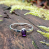 sterling silver stacking ring with  Purple oval amethyst, sitting on a mossy log in the sun