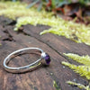 sterling silver stacking ring with  Purple oval amethyst, sitting on a mossy log in the sun