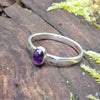 sterling silver stacking ring with  Purple oval amethyst, sitting on a mossy log in the sun
