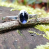 sterling silver stacking ring with Deep bluish Purple oval iolite, sitting on a mossy log in the sun. 