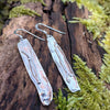 Medium slim melt drop silver earrings on a mossy log