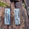 long melt textured silver studs sitting on a mossy log in the sunshine.