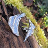 Odd irregular curved triangle shaped melt textured silver studs sitting on a mossy log in the sunshine.