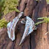 Odd irregular curved triangle shaped melt textured silver studs sitting on a mossy log in the sunshine.