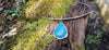 Blue stone pendant with silver tendrils on a silver bar and chain sits on a mossy log