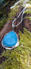 Blue stone pendant with silver tendrils on a long silver chain sits on a mossy log