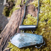 Oxidised silver pendant with coffin shaped  moss agate stone on a chunky chain. Sitting on a mossy log 