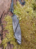 Oxidised silver pendant with a long oval Labradorite stone and a chunky chain sitting on a mossy log.  Back view showing tendril detail.
