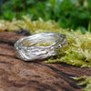 A sterling silver wound strand ring sits on a mossy log 