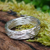 A sterling silver wound strand ring sits on a mossy log 