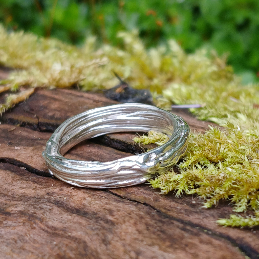 A sterling silver wound strand ring sits on a mossy log 