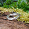A sterling silver wound strand ring sits on a mossy log 
