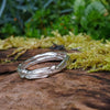 A sterling silver wound strand ring sits on a mossy log 