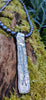 Long Straight sterling silver melt textured pendant on black freshwater pearl beads. the necklace lies on a mossy woodland log.