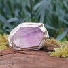 Silver ring with large uncut pale lavender Amethyst sits on a mossy log in the sunshine