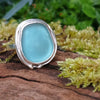 Sterling silver ring with a turquoise oval ish shaped sea glass stone. Sitting on a mossy log in the sunshine.