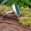 Sterling silver ring with a turquoise oval ish shaped sea glass stone. Sitting on a mossy log in the sunshine.