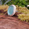 Sterling silver ring with a turquoise oval ish shaped sea glass stone. Sitting on a mossy log in the sunshine.