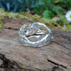 A wibbly wobbly  holey molten textured silver ring sits on a mossy log with leaves in the backround.