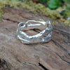 A wibbly wobbly  holey molten textured silver ring sits on a mossy log with leaves in the backround.