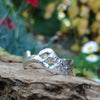 A second wibbly wobbly  holey molten textured silver ring sits on a mossy log with leaves in the backround.