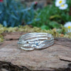 A third molten textured silver ring sits on a mossy log with leaves in the backround. This one has wound and overlapping melted stands.