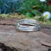 A third molten textured silver ring sits on a mossy log with leaves in the backround. This one has wound and overlapping melted stands.
