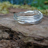 A third molten textured silver ring sits on a mossy log with leaves in the backround. This one has wound and overlapping melted stands.