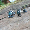 Oxidised finish sterling silver and moss agate stud earrings with tiny tendril wrapping around the stone, sitting on a mossy log in the sunshine.