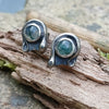 Oxidised finish sterling silver and moss agate stud earrings with tiny tendril wrapping around the stone, sitting on a mossy log