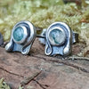 Oxidised finish sterling silver and moss agate stud earrings with tiny tendril wrapping around the stone, sitting on a mossy log in the sunshine.
