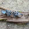 Bud shaped labradorite stones with tangled tendril tails. oxidised silver stud earrings with a dreamy elfin quality sits on a weathered piece of wood, the labradorite stones glinting blue in the sunlight. Shown with the buds facing outwards and the tendrins facing in.