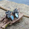 Bud shaped labradorite stones with tangled tendril tails. oxidised silver stud earrings with a dreamy elfin quality sits on a weathered piece of wood, the labradorite stones glinting blue in the sunlight. Shown with the buds facing down and the tendrils up.