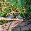 Leaf shaped labradorite stones with silver stems. oxidised silver stud earrings with a dreamy elfin quality sits on a weathered piece of wood, the labradorite stones glinting blue in the sunlight. Shown with the leaves facing inwards and the stems facing in facing out.