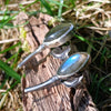 Leaf shaped labradorite stones with silver stems. oxidised silver stud earrings with a dreamy elfin quality sits on a weathered piece of wood, the labradorite stones glinting blue in the sunlight. Side on to show the large butterfly closures.