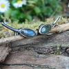Leaf shaped labradorite stones with silver stems. oxidised silver stud earrings with a dreamy elfin quality sits on a weathered piece of wood, the labradorite stones glinting blue in the sunlight. Shown with the leaves facing inwards and the stems facing in facing out.