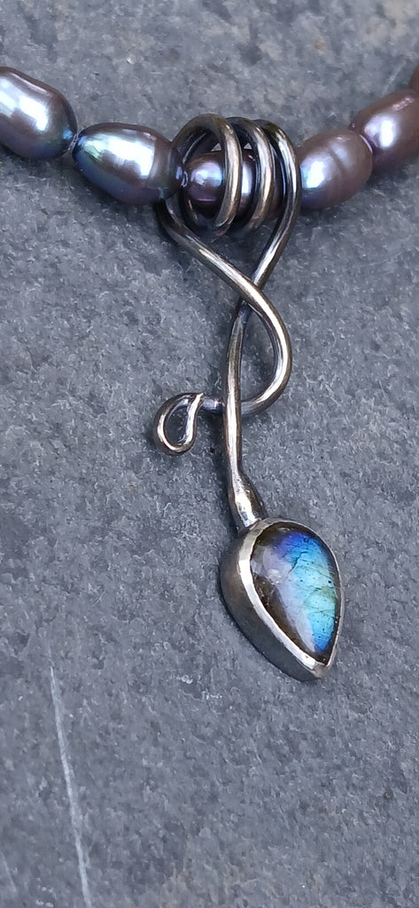 an oxidised silver tendril pendant wraps up and around the black freshwater pearls and down to the bud shaped blue flash labradorite.
on a slate background.