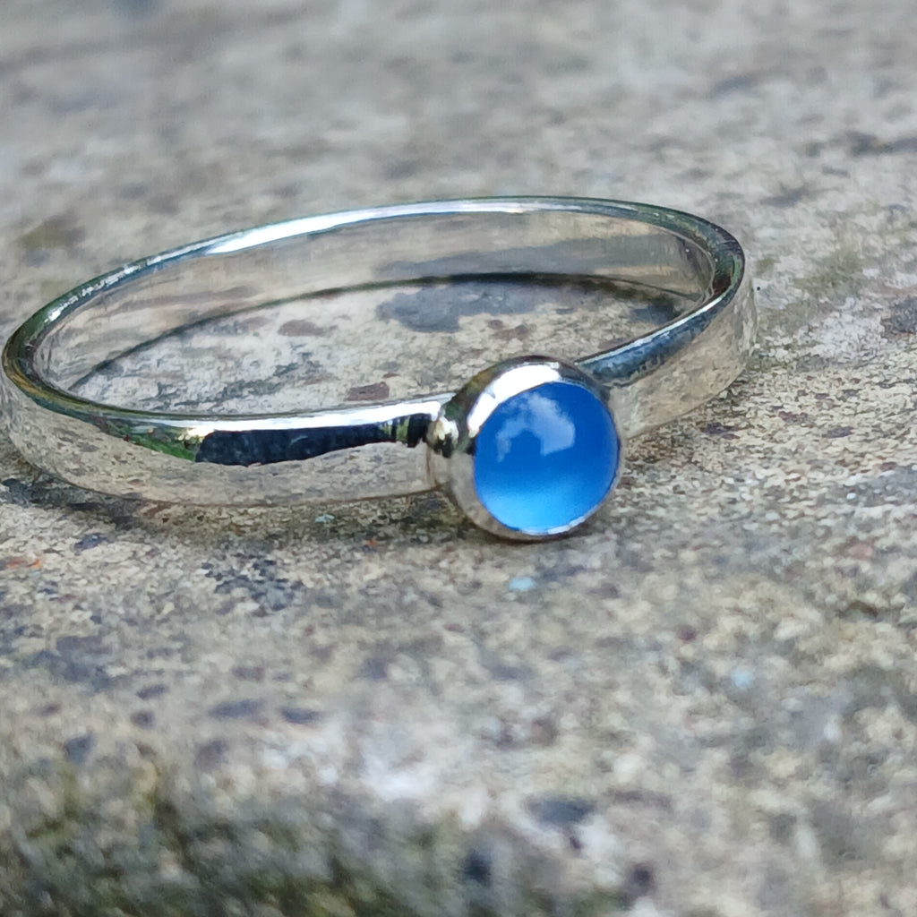 A sterling silver ring with a round, bezel-set blue onyx gemstone, photographed close-up against a textured gray stone background.