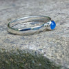 A sterling silver ring with a round, bezel-set blue onyx gemstone, photographed close-up against a textured gray stone background.