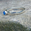 A sterling silver ring with a round, bezel-set blue onyx gemstone, photographed close-up against a textured gray stone background.