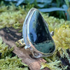Sterling silver ring with a large green freeform oval Nebula Jasper stone surrounded with tendrils. The ring sits on a mossy log.