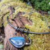 Oxidised black silver tendril pendant with blue flash labradorite bud winds around a bar and chain neckwire. Pictured on a mossy log