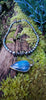 Oxidised black silver tendril pendant with blue flash labradorite bud winds around black oval freshwater pearls. Pictured on a mossy log. 