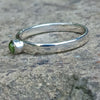 A sterling silver ring with a round, bezel-set green Peridot gemstone, photographed close-up against a textured gray stone background.
